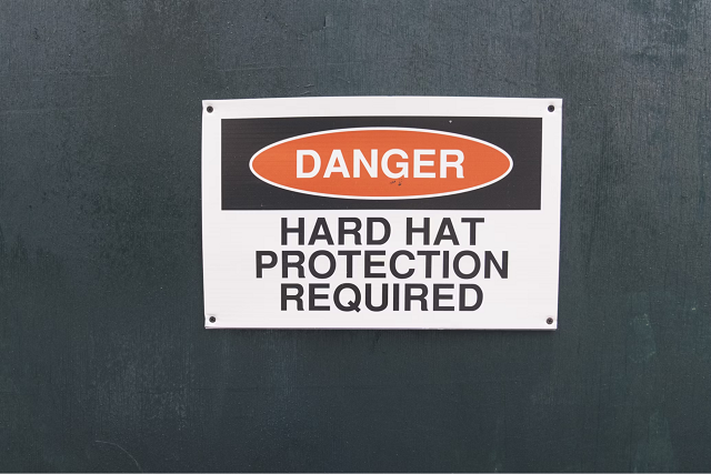 Metal sign attached to wall or equipment that says "Danger Hard Hat Protection Required"